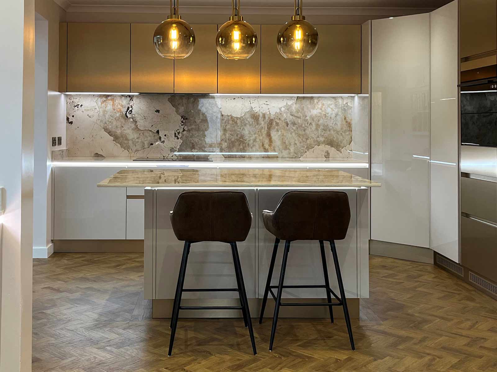 A light grey cashmere kitchen with handleless units and a gold splashback