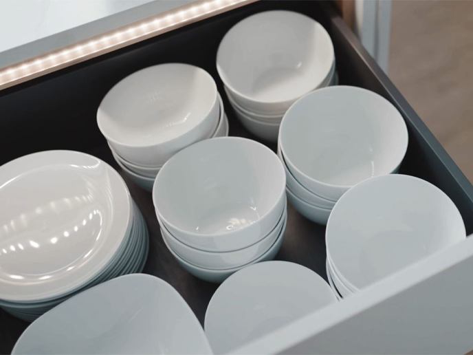 A handleless pan drawer with a gold handle rail and strip lighting