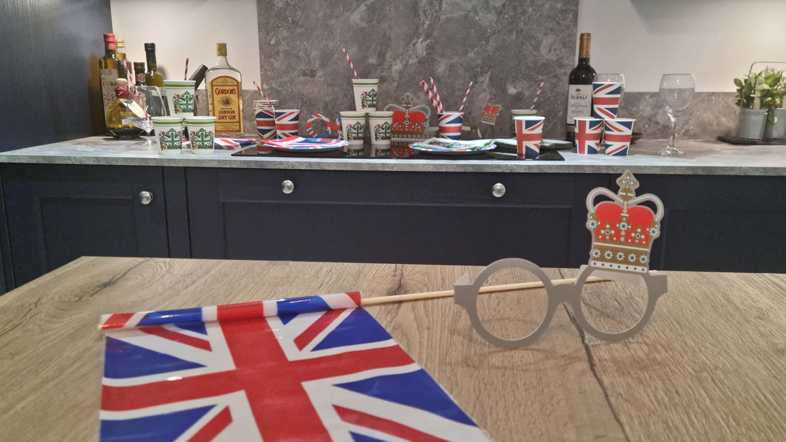A union jack flag and royal novelty glasses with a dark blue Shaker kitchen